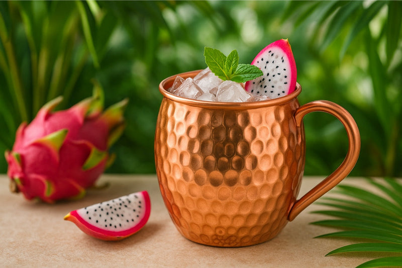 Erfrischender Drachenfrucht-Cocktail mit Eiswürfeln serviert in einem glänzenden Kupferbecher auf einem sommerlich gedeckten Holztisch
